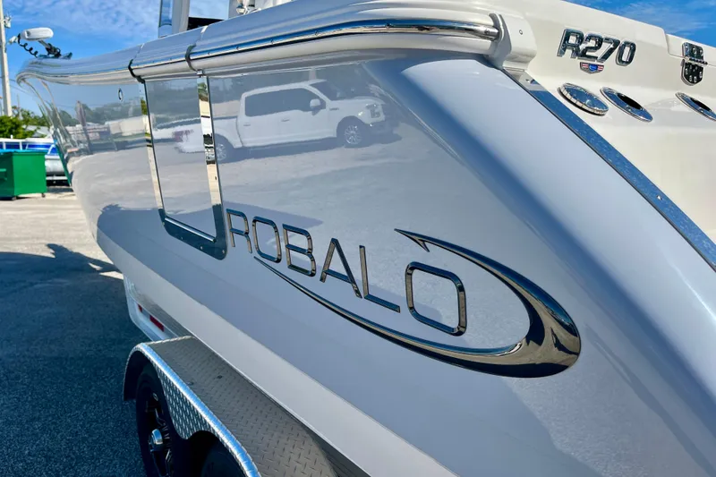 Slide: The Image of 2026 Robalo R270 Center Console boat, sleek design with chrome accents, parked outdoors. - 11