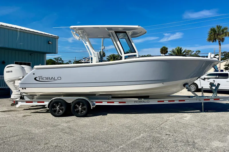 Slide: The Image of 2026 Robalo R270 Center Console boat on trailer, parked outdoors under clear blue sky. - 5