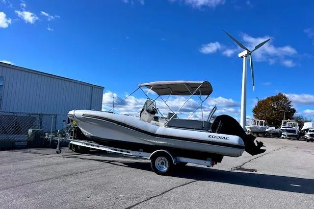 The Image of 2023 Zodiac N-ZO 680 boat on trailer, parked near wind turbine under clear blue sky. - 0