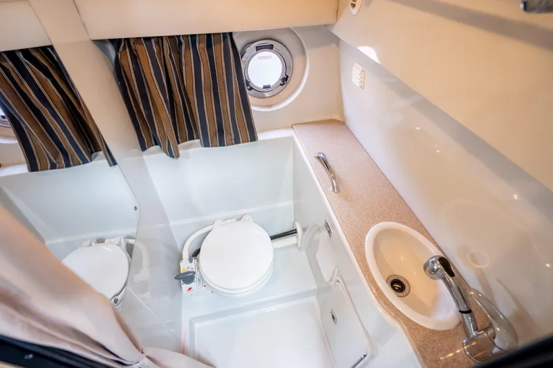Slide: The Image of 2015 Crownline 294 CR boat bathroom with toilet, sink, and striped curtains. - 22
