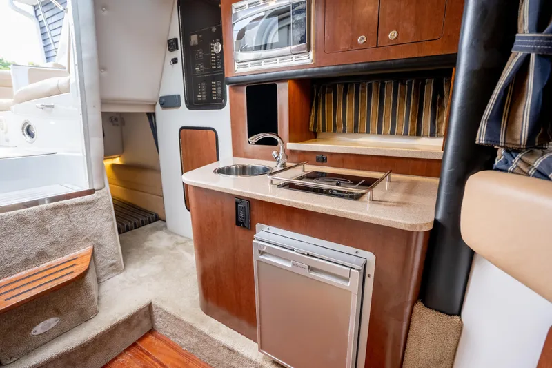 Slide: The Image of 2015 Crownline 294 CR boat interior with kitchenette, featuring sink, stove, and microwave. - 17