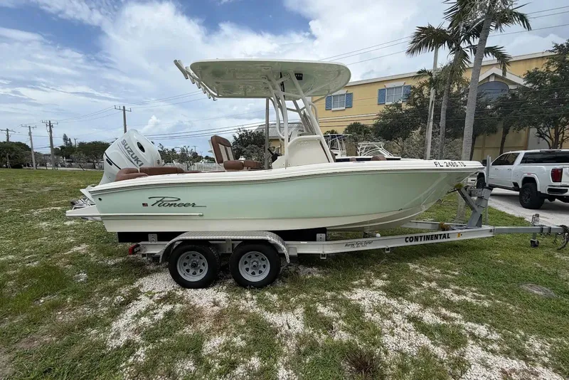 Slide: The Image of 2023 Pioneer 202 Islander boat on trailer, parked outdoors with palm trees and buildings nearby. - 1