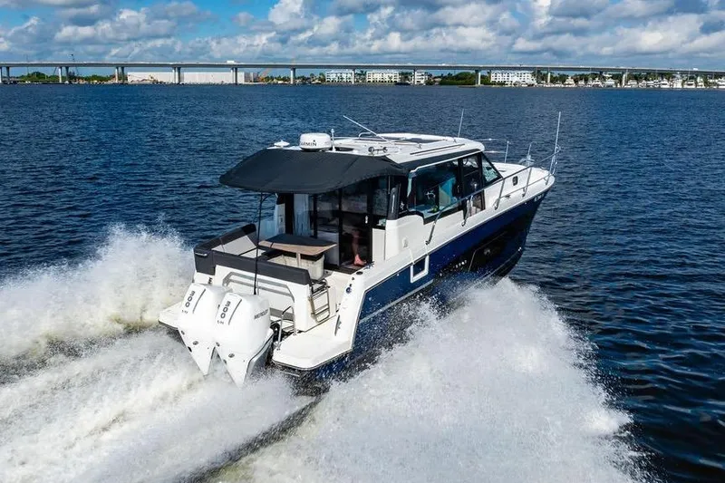 Slide: The Image of 2023 Jeanneau NC 1095 cruising on open water with cityscape in background. - 8