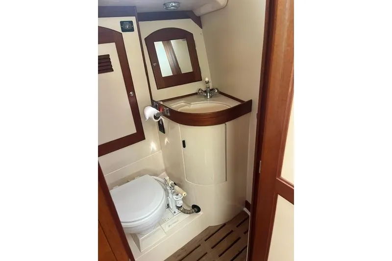 Slide: The Image of Compact boat bathroom with wooden accents, featuring a toilet, sink, and mirror. Sabre 452, 2002 model. - 28