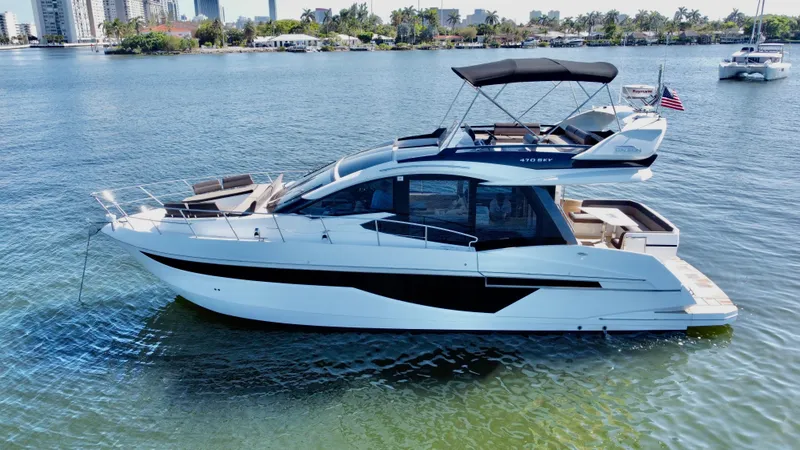 Slide: The Image of 2022 Galeon 470 Sky yacht cruising on a calm waterway with cityscape in the background. - 2
