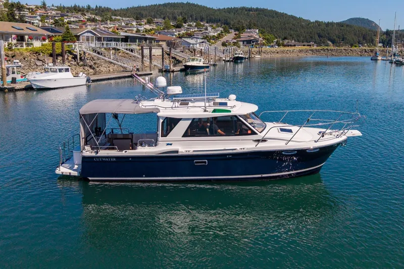 The Image of 2015 Cutwater 28 boat docked in a scenic marina with waterfront homes. - 0