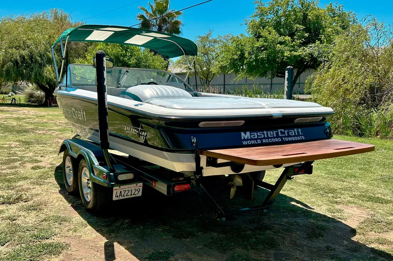Slide: The Image of 2002 MasterCraft ProStar 197 boat on trailer, parked on grass with trees in background. - 2