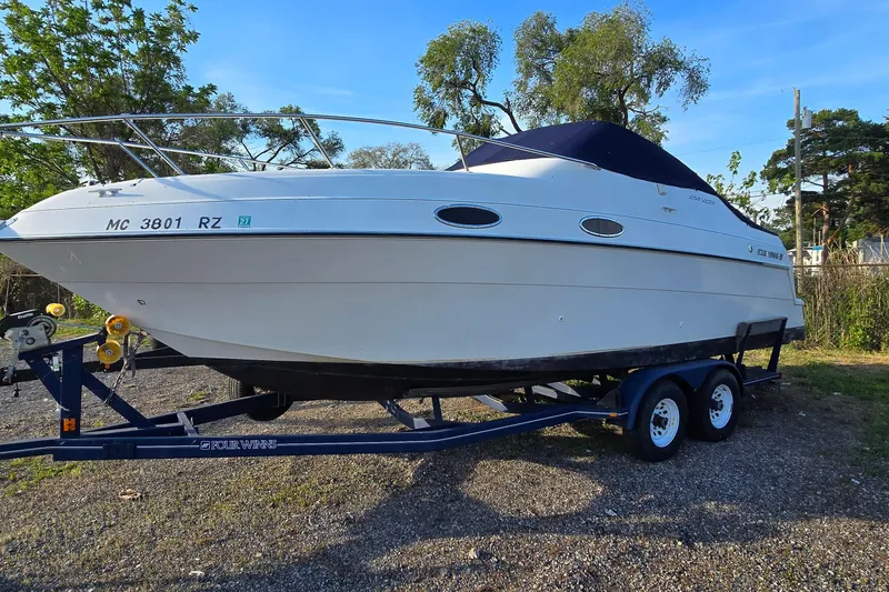 The Image of 1999 Four Winns 258 Vista boat on trailer, parked outdoors, surrounded by trees. - 1