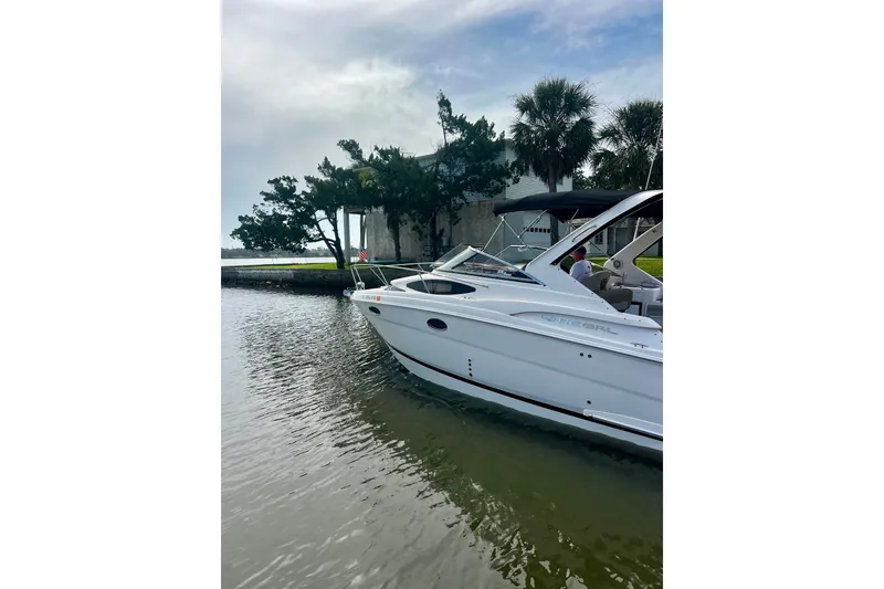 The Image of A white 2015 Regal 30 Express boat is docked on calm water with trees in the background. - 0