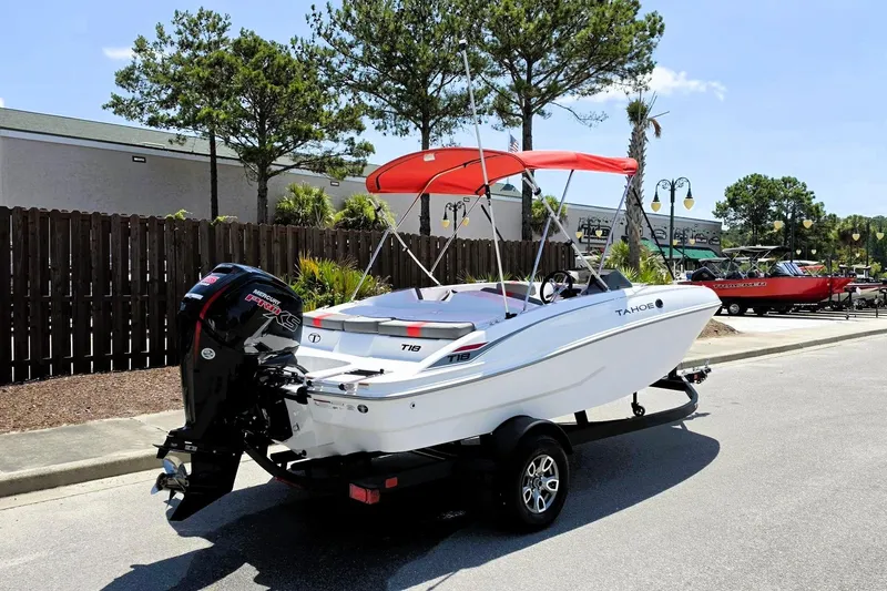 Slide: The Image of 2026 Tahoe T18 boat with red canopy on trailer, parked outdoors. - 2