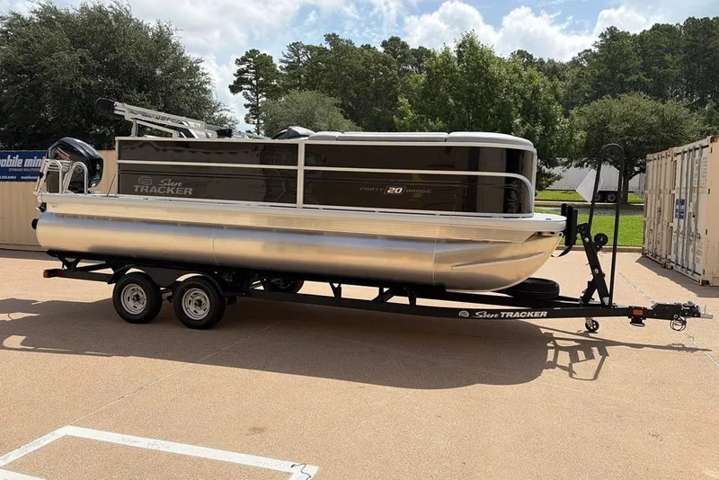 Slide: The Image of 2026 Sun Tracker Party Barge 20 DLX pontoon boat on trailer, parked outdoors. - 2
