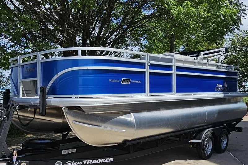 The Image of 2026 Sun Tracker Fishin' Barge 20 DLX pontoon boat on trailer, parked under trees. - 0