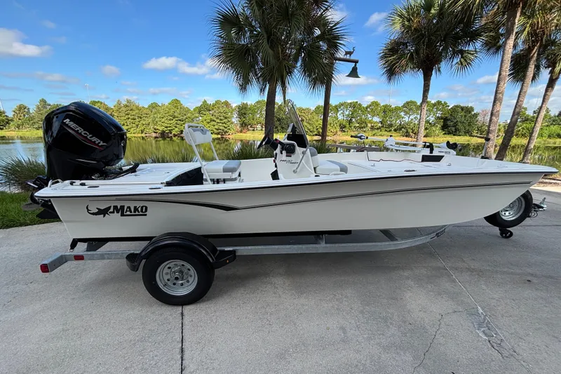 Slide: The Image of 2026 Mako Pro Skiff 17 CC boat on trailer, parked near a scenic lake. - 1