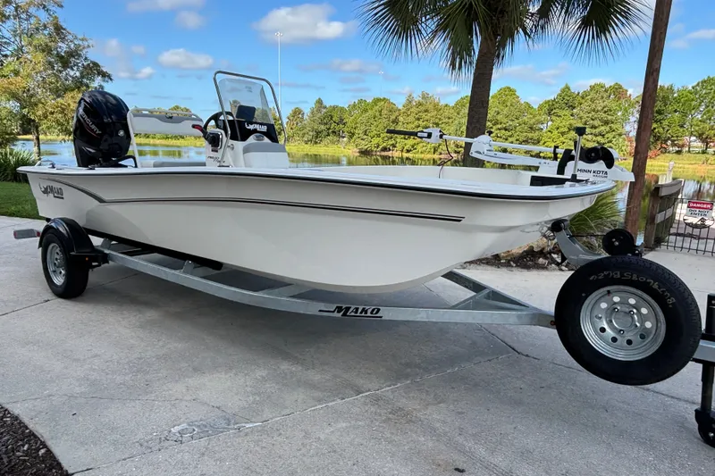Slide: The Image of 2026 Mako Pro Skiff 17 CC boat on trailer, parked near a scenic lake. - 0