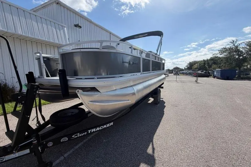 Slide: The Image of 2026 Sun Tracker Bass Buggy 18 DLX pontoon boat on trailer, parked outdoors. - 2