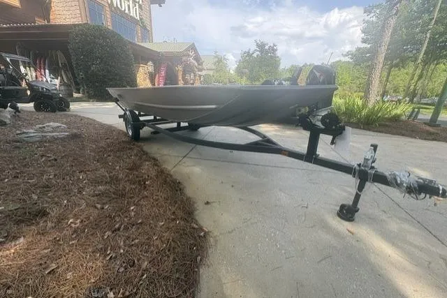 Slide: The Image of 2026 Tracker Grizzly 1754 Utility boat on trailer outside a store, surrounded by trees. - 3