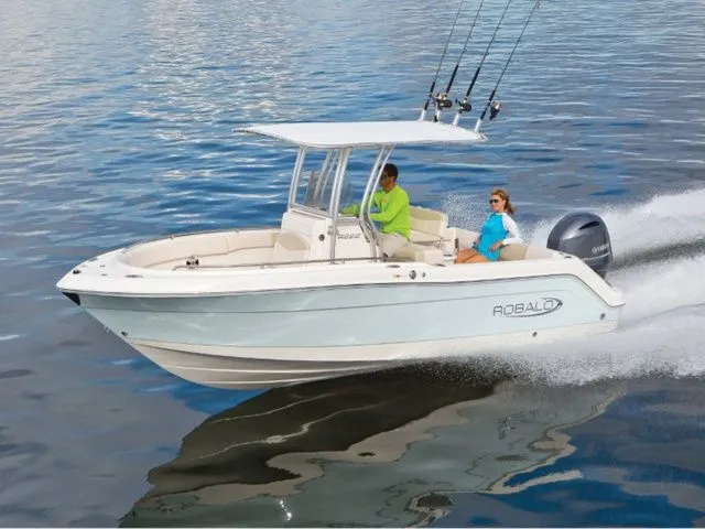 The Image of A 2020 Robalo R222 boat speeds across calm water. Two people are seated onboard. - 1