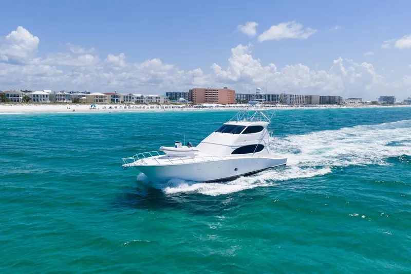 Slide: The Image of 2008 Hatteras 77 Convertible yacht cruising in turquoise waters near a coastal city. - 19