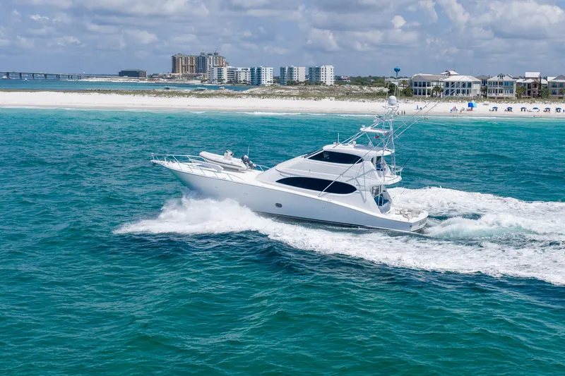 Slide: The Image of 2008 Hatteras 77 Convertible yacht cruising in turquoise waters near a sandy beach. - 4