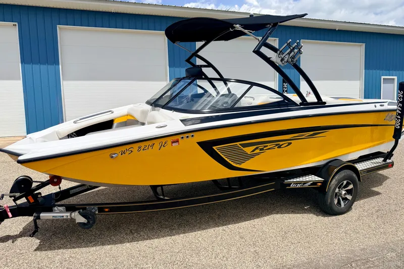 Slide: The Image of 2014 Tigé R20 yellow boat on trailer, parked near blue building. - 6