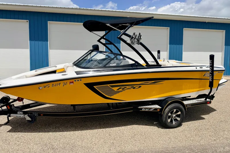 Slide: The Image of 2014 Tigé R20 yellow boat on trailer, parked outside blue building. - 4