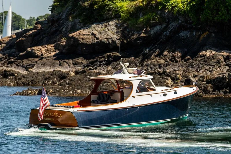Slide: The Image of Hinckley Picnic Boat 36 Classic, 2000 model, cruising near rocky shoreline with American flag. - 2