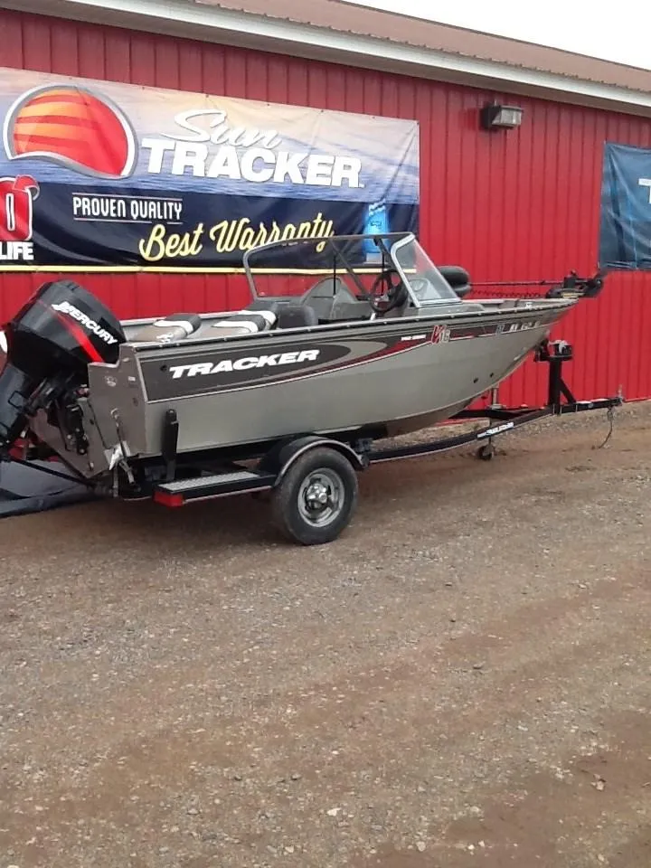 The Image of 2005 Tracker Pro Guide V-16 WT boat on trailer in front of red building. - 0