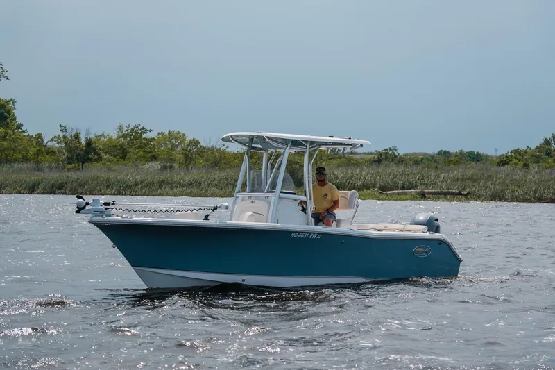 Slide: The Image of 2022 Sea Hunt Ultra 229 boat cruising on a calm river with lush greenery in the background. - 2