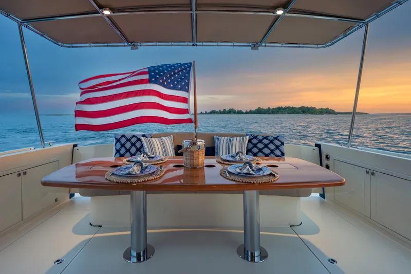 Slide: The Image of 2018 Palm Beach Motor Yachts 55, elegant dining setup, American flag, sunset ocean view. - 12