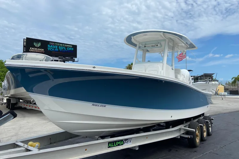The Image of 2027 Regulator 26XO boat on trailer, blue hull, parked outdoors under cloudy sky. - 1