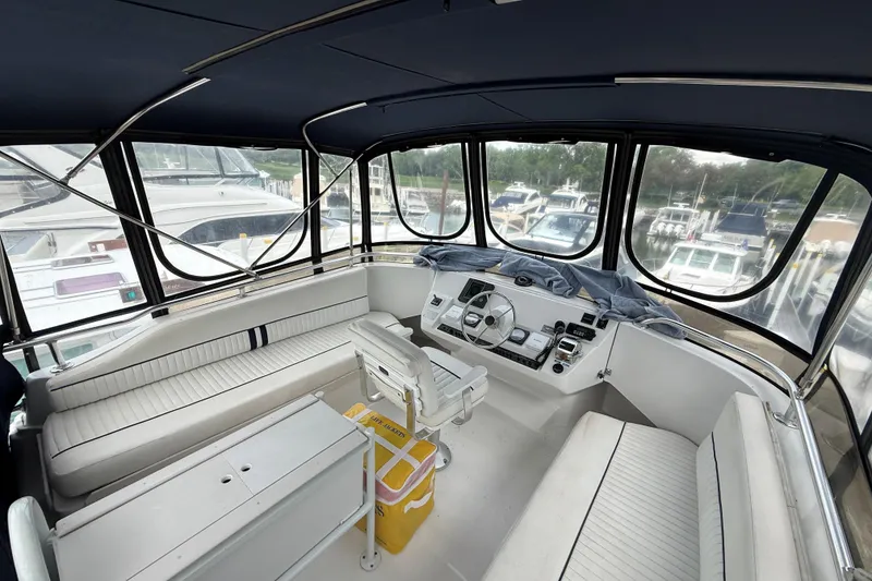 Slide: The Image of 1999 Mainship 350 Trawler helm with panoramic marina view, featuring white seating and controls. - 13