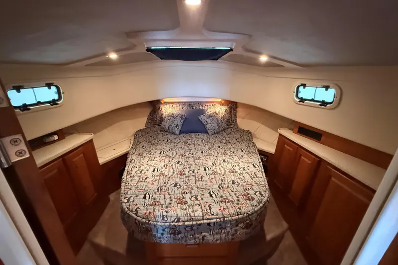 Slide: The Image of 1999 Mainship 350 Trawler cabin with cozy bed, wooden cabinets, and porthole windows. - 25