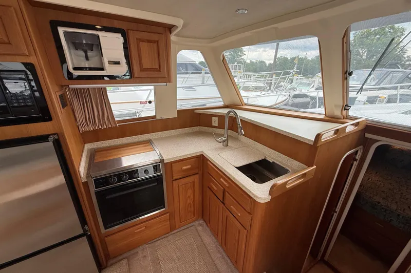 Slide: The Image of 1999 Mainship 350 Trawler kitchen with wood cabinetry, stainless steel appliances, and large windows. - 19