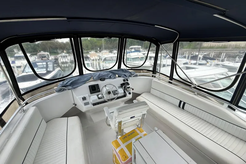 Slide: The Image of 1999 Mainship 350 Trawler interior with helm, seating, and marina view. - 15