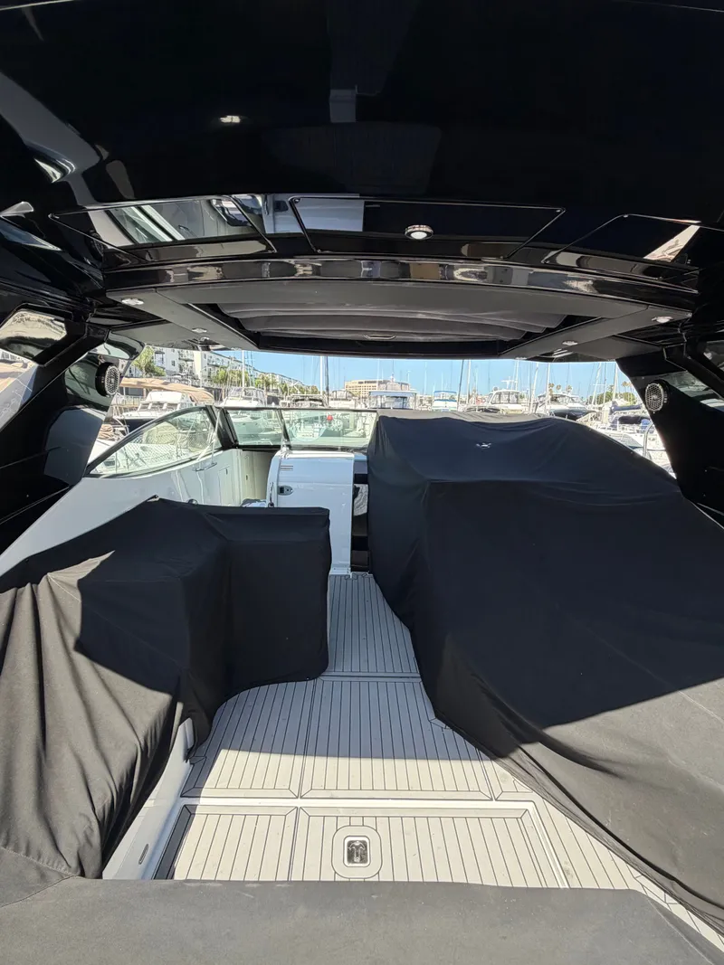 Slide: The Image of The image shows the cockpit of a 2021 Cruisers Yachts 38 GLS. It features a modern, open design with covers over the seating. Boats are visible in the harbor background. - 7