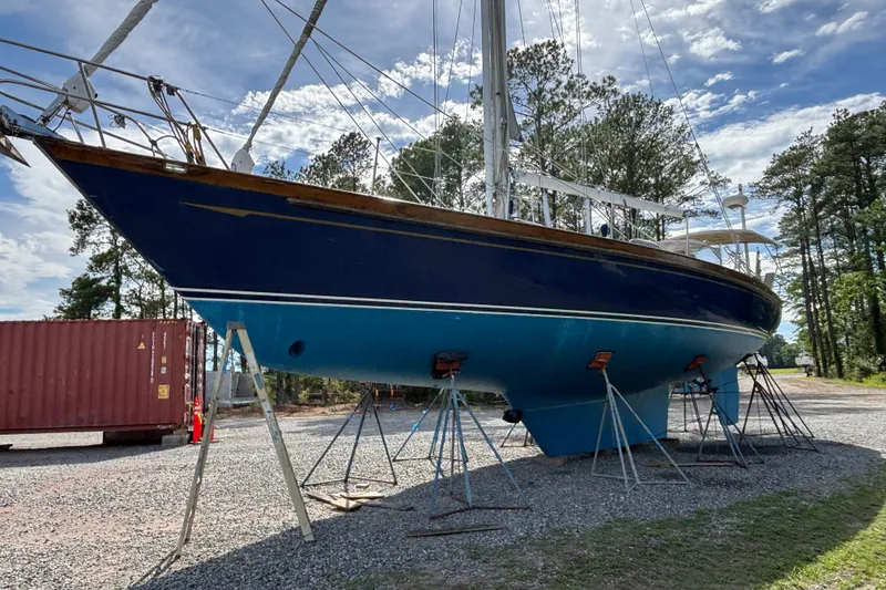 Slide: The Image of 1988 Tayana 52 sailboat on stands, blue hull, outdoors, clear sky, trees in background. - 11