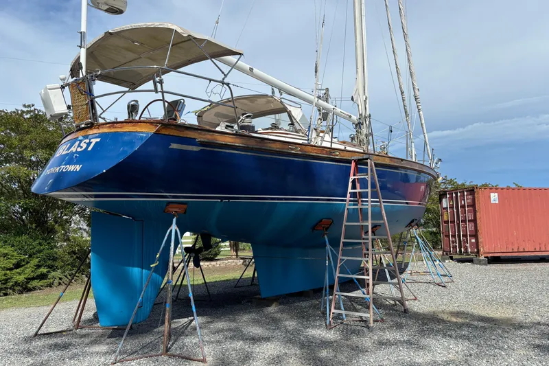 Slide: The Image of 1988 Tayana 52 sailboat on stands, blue hull, outdoor setting, with ladders and container nearby. - 14