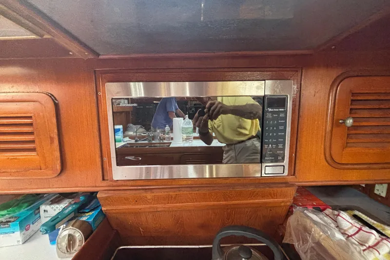 Slide: The Image of Microwave in 1988 Tayana 52 yacht kitchen with wooden cabinetry and reflection. - 54