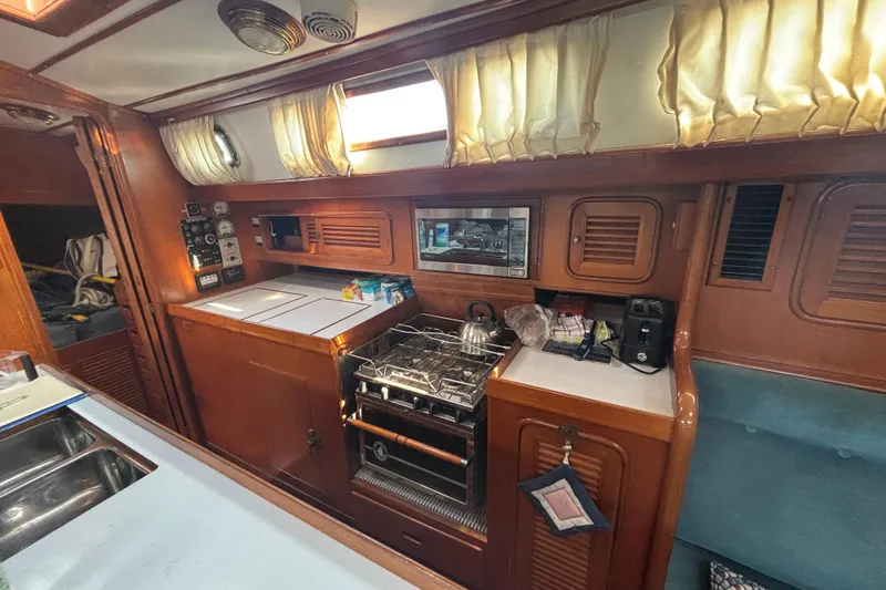 Slide: The Image of Interior of 1988 Tayana 52 yacht kitchen with stove, microwave, and wooden cabinetry. - 52
