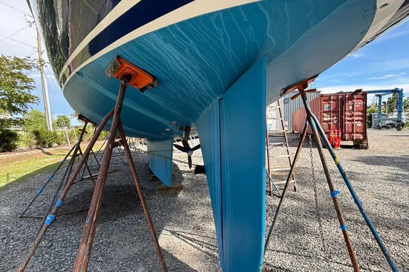 Slide: The Image of 1988 Tayana 52 sailboat hull on stands, blue paint, outdoor storage area. - 16