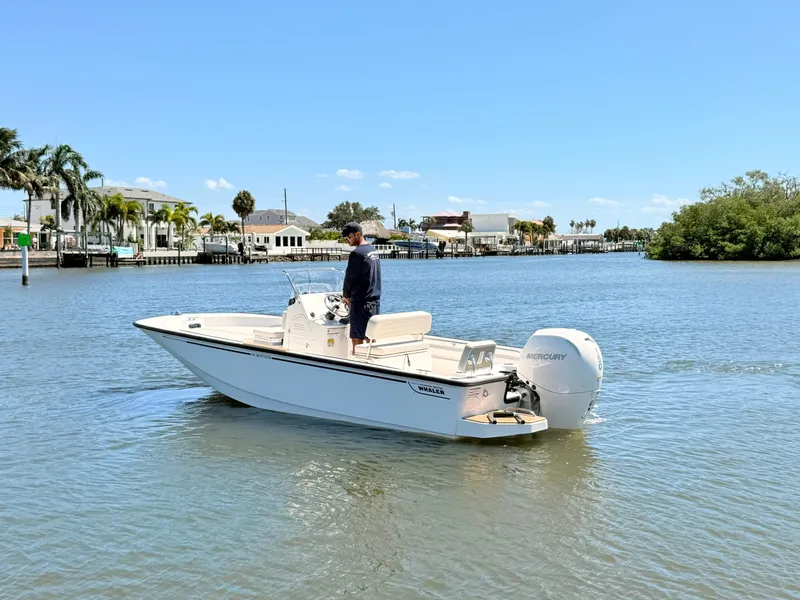 Slide: The Image of A 2027 Boston Whaler 190 Montauk on calm water. A man stands at the helm. - 14