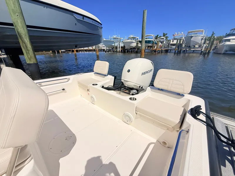 Slide: The Image of The image shows the cockpit of a 2027 Boston Whaler 190 Montauk. It features a clean, white deck with a Mercury outboard motor. Several boats are visible docked in the background. - 18