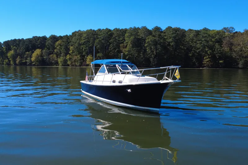 The Image of 2003 Mainship Pilot 30-II boat on calm lake with forested shoreline. - 0