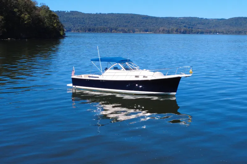 Slide: The Image of 2003 Mainship Pilot 30-II boat on a serene lake with forested hills in the background. - 2