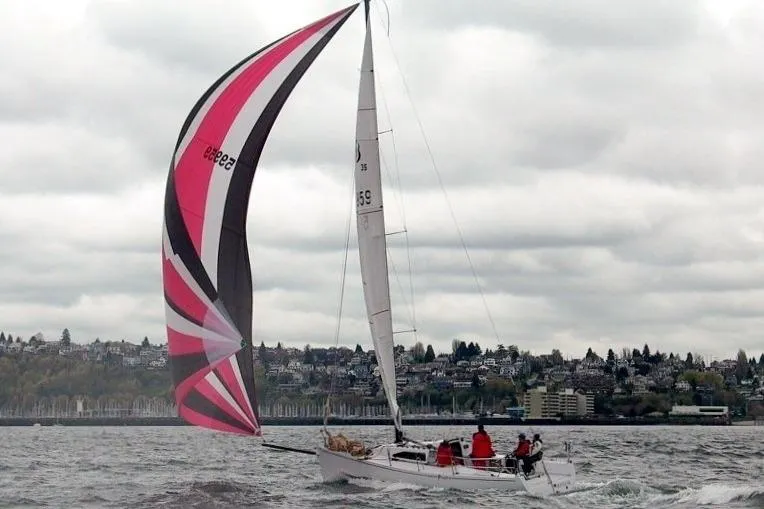 The Image of Sailboat Bravura B35 (1999) with colorful spinnaker sailing on a cloudy day near shoreline. - 0