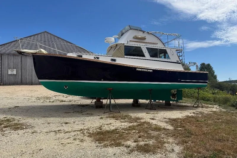 The Image of 1995 Wilbur Weekender boat on stands, blue hull, green bottom, outdoor setting. - 0