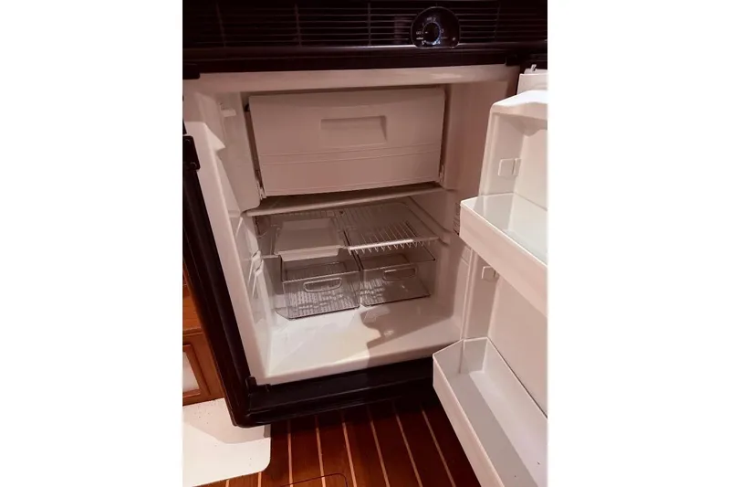 Slide: The Image of Open refrigerator inside a 1995 Wilbur Weekender boat, featuring empty shelves and compartments. - 24