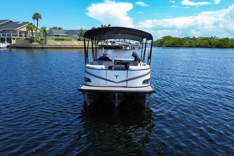 Slide: The Image of 2025 Tahoe Pontoon LTZ 23 on a serene lake, featuring a sleek design and canopy. - 2