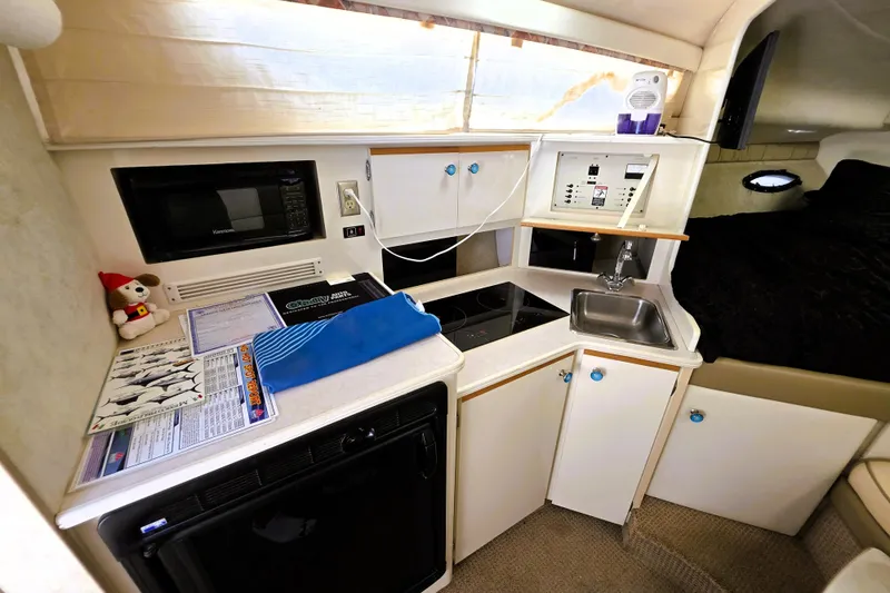 Slide: The Image of 1999 Bayliner 3055 Ciera cabin interior with kitchenette, featuring microwave, sink, and storage cabinets. - 11