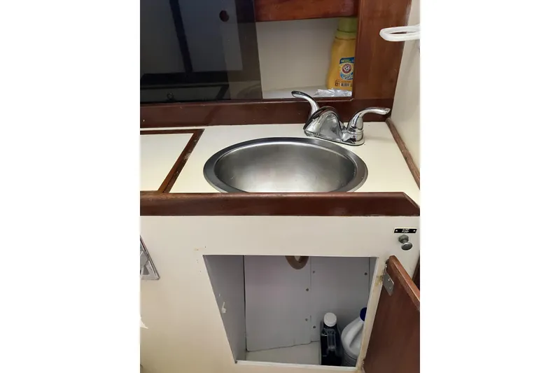 Slide: The Image of 1981 Pearson 365 Ketch boat sink area with wooden cabinetry and cleaning supplies. - 30